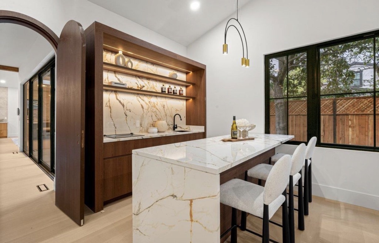 Custom walnut entertaining bar with illuminated stone backsplash and waterfall island