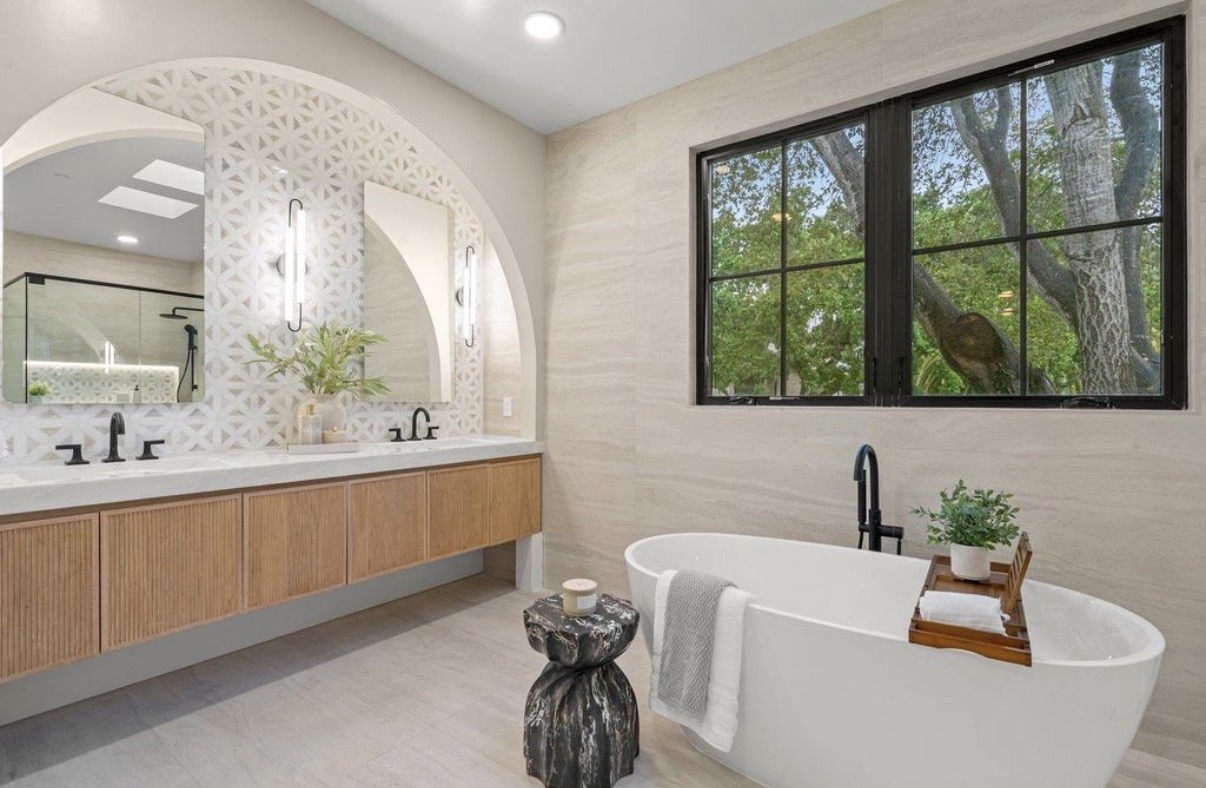 Serene primary bathroom with arched vanity, soaking tub and garden view