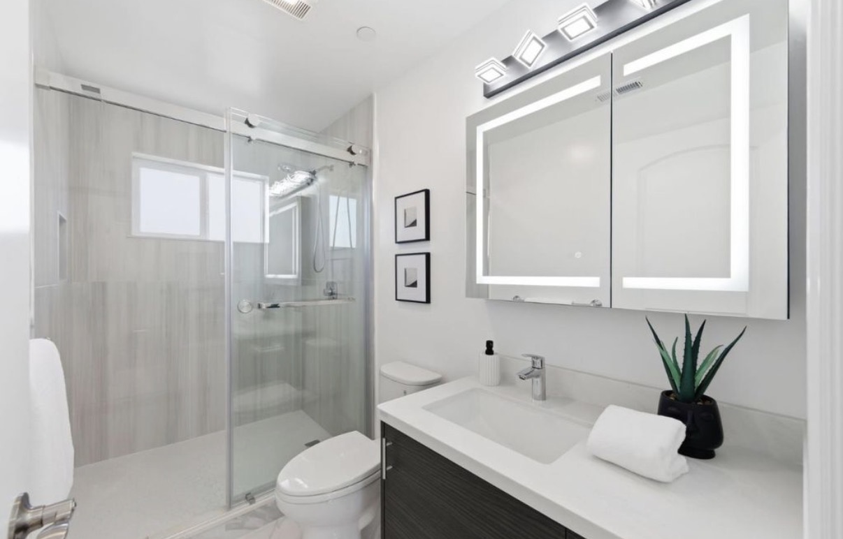 Bright modern bathroom with illuminated mirrored cabinetry and glass shower